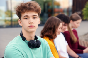 Boy with headphones on his own with friends behind him - Understanding my Autism